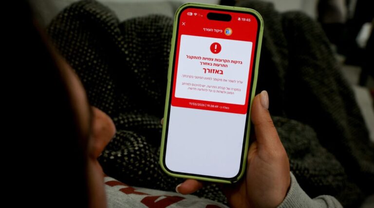 A woman shows a missile alert notification on her mobile phone as residents take cover indoors following missile fire from Iran toward Israel, in Mishmar David, March 11. 2026. Photo by Nati Shohat/Flash90